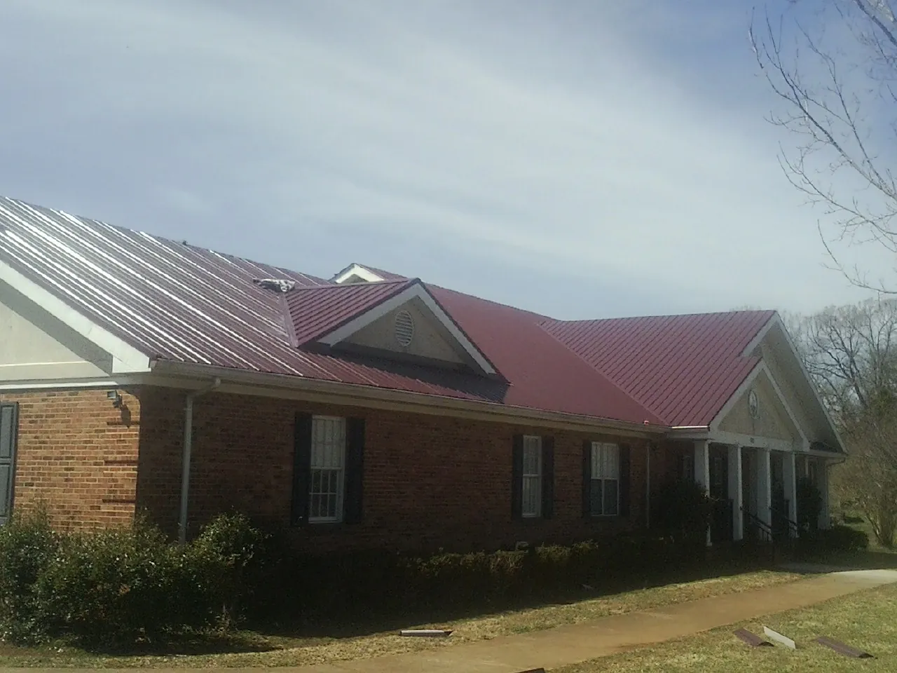 Red metal roof with gabled entries on a long brick building, from a Hail Damage Roof Repair job in Tavares