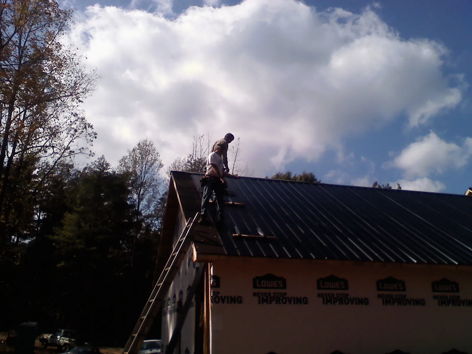 Roofer fastening dark metal panels high against a cloudy sky, from a Roof Inspection job in Tavares