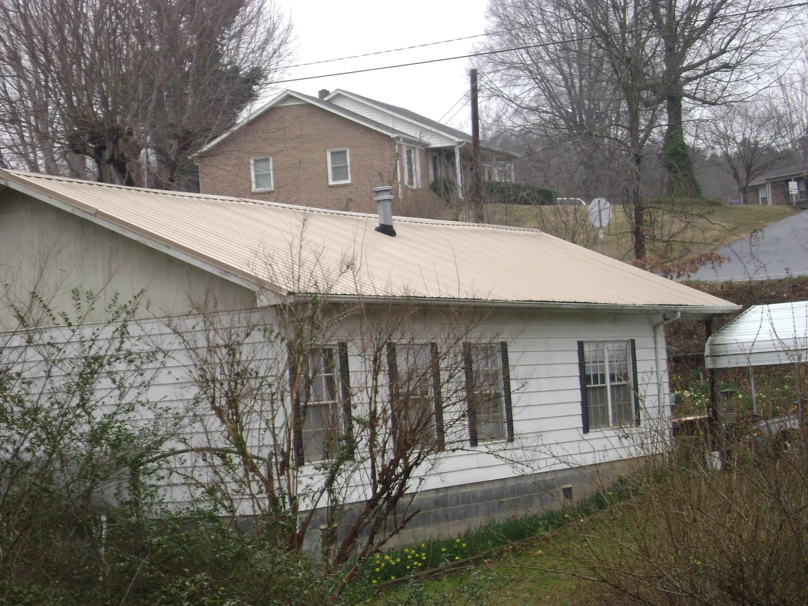 Tan metal roof on a white sided house set into a hillside — Commercial Roofing by Roofing Brothers in Tavares